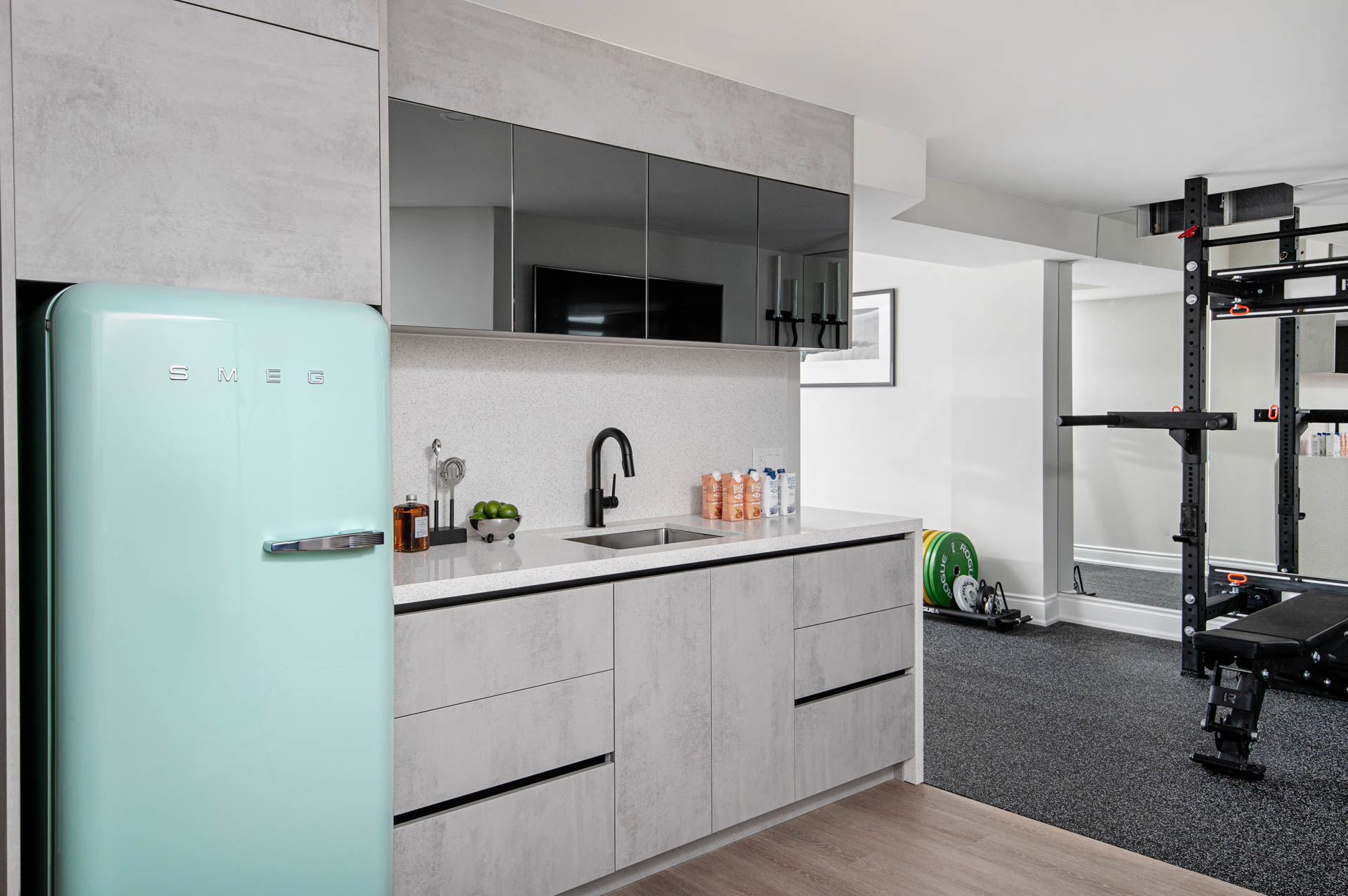 Image of a modern basement bar, showcasing slab concrete look drawers and black mirror upper cabinets, mint smeg fridge.