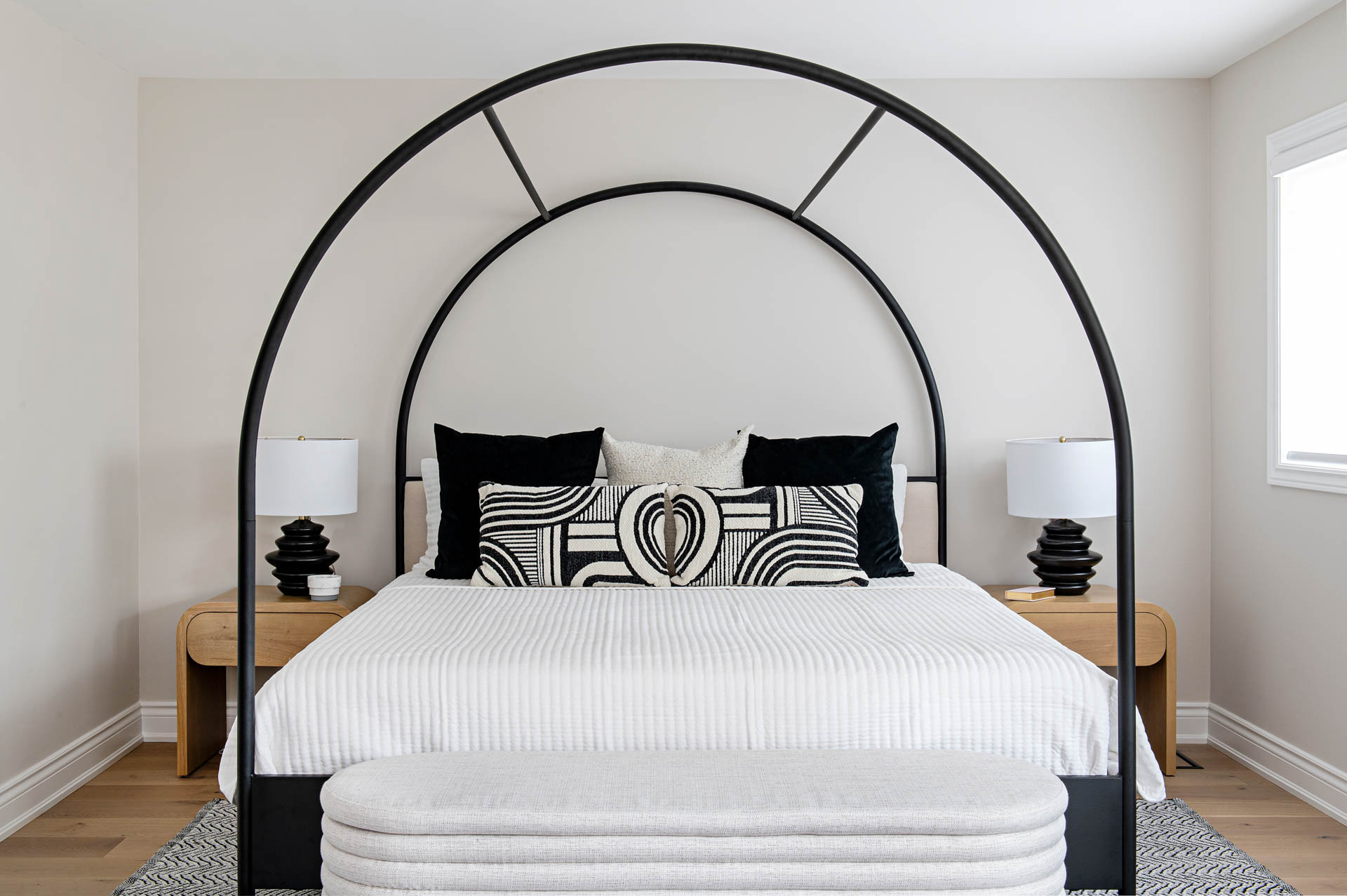 Image of Black and White Decor Primary Bedroom, black metal arched canopy bed with natural wood side tables, black table lamps.