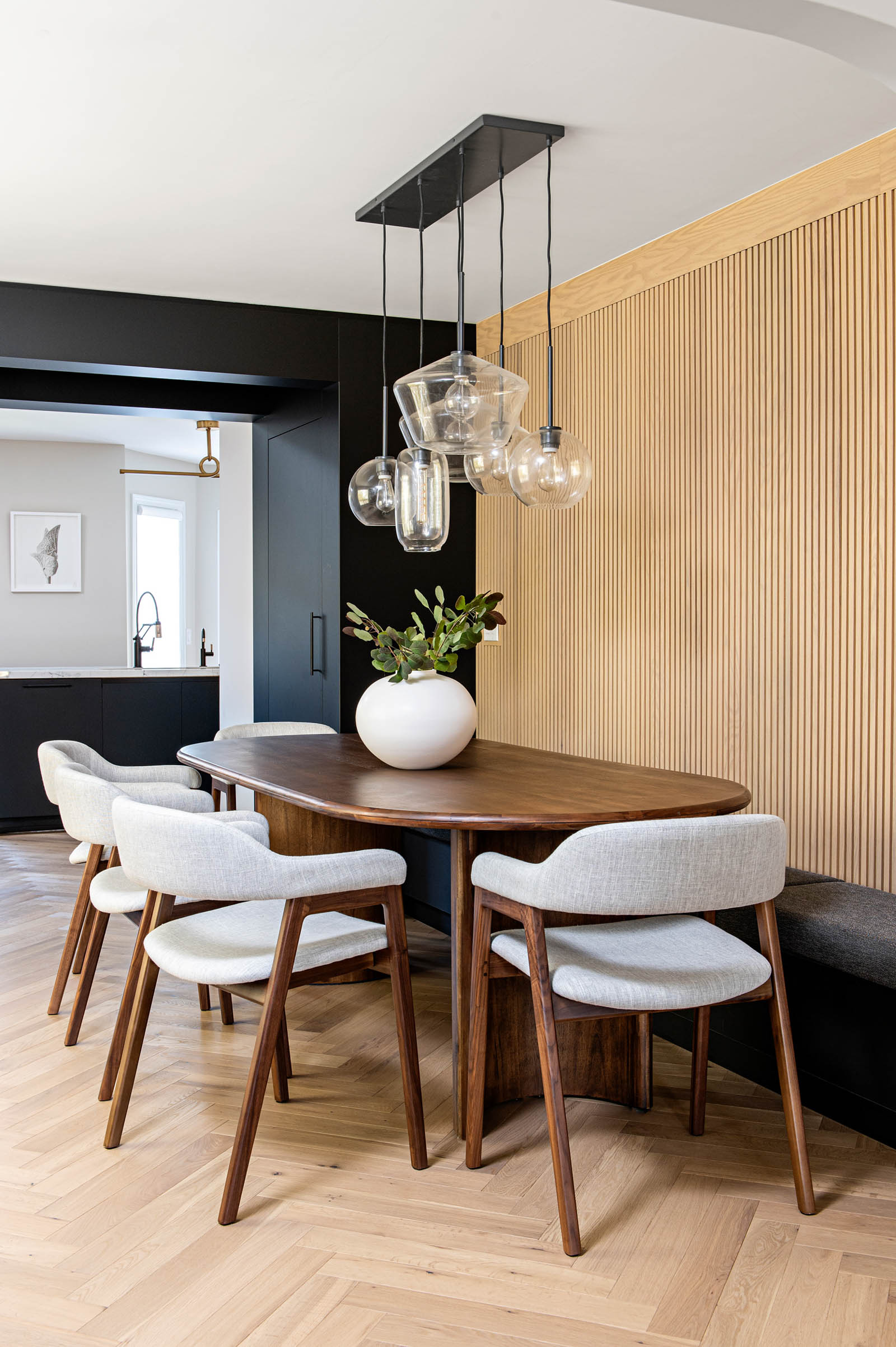 Image of Modern dining room with custom bench seating, natural oak reeded wall, solid wood table, and upholstered dining chairs with wood legs.