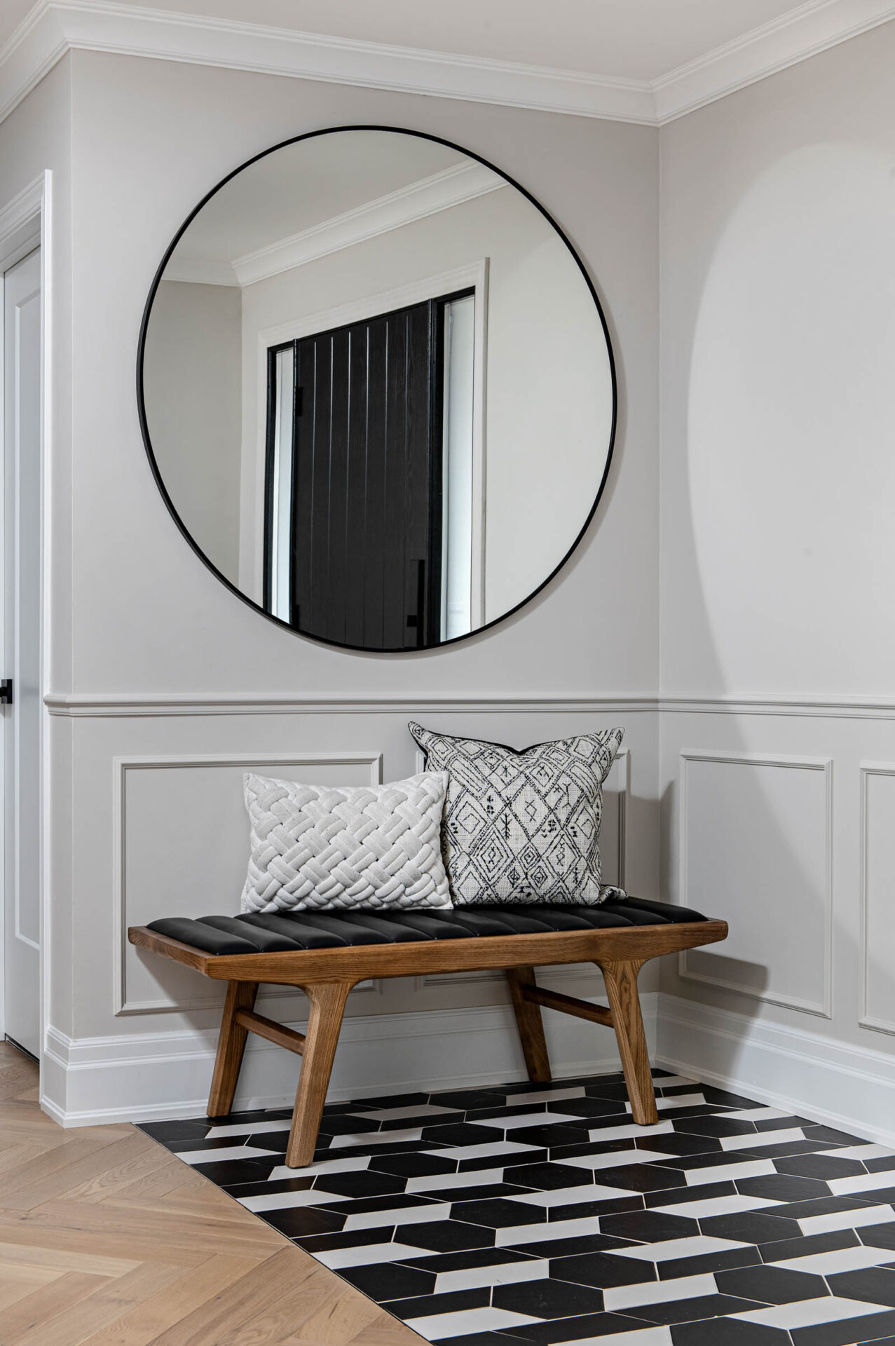 Image of front entrance with bench and large round mirror, black and white geometric patterned tile floor.