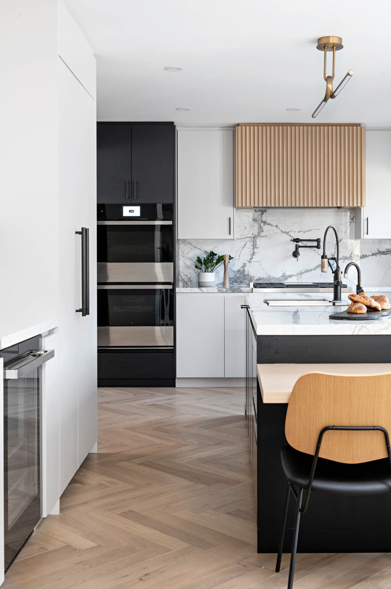 Image of a Contemporary kitchen with marble look porcelain countertop and Backsplash, light grey slab cabinets and drawers, Natural Wood Reeded hood fan, Large island with cantilevered table.