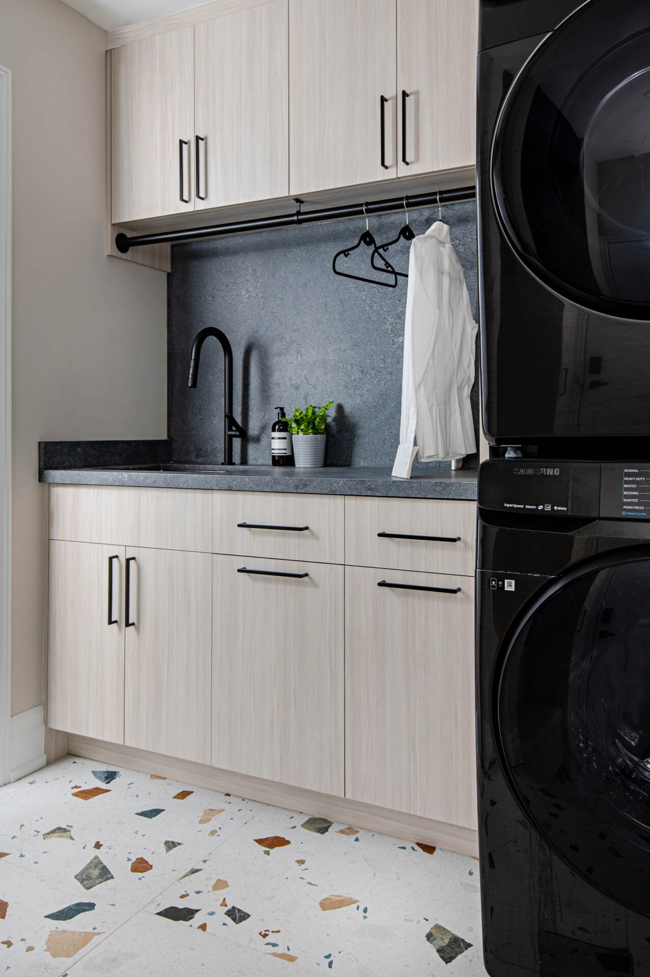 Image of a modern Laundry Room showcasing custom cabinetry, slab doors with black modern hardware. Concrete quartz and backsplash. Large scale terrazzo porcelain tile.