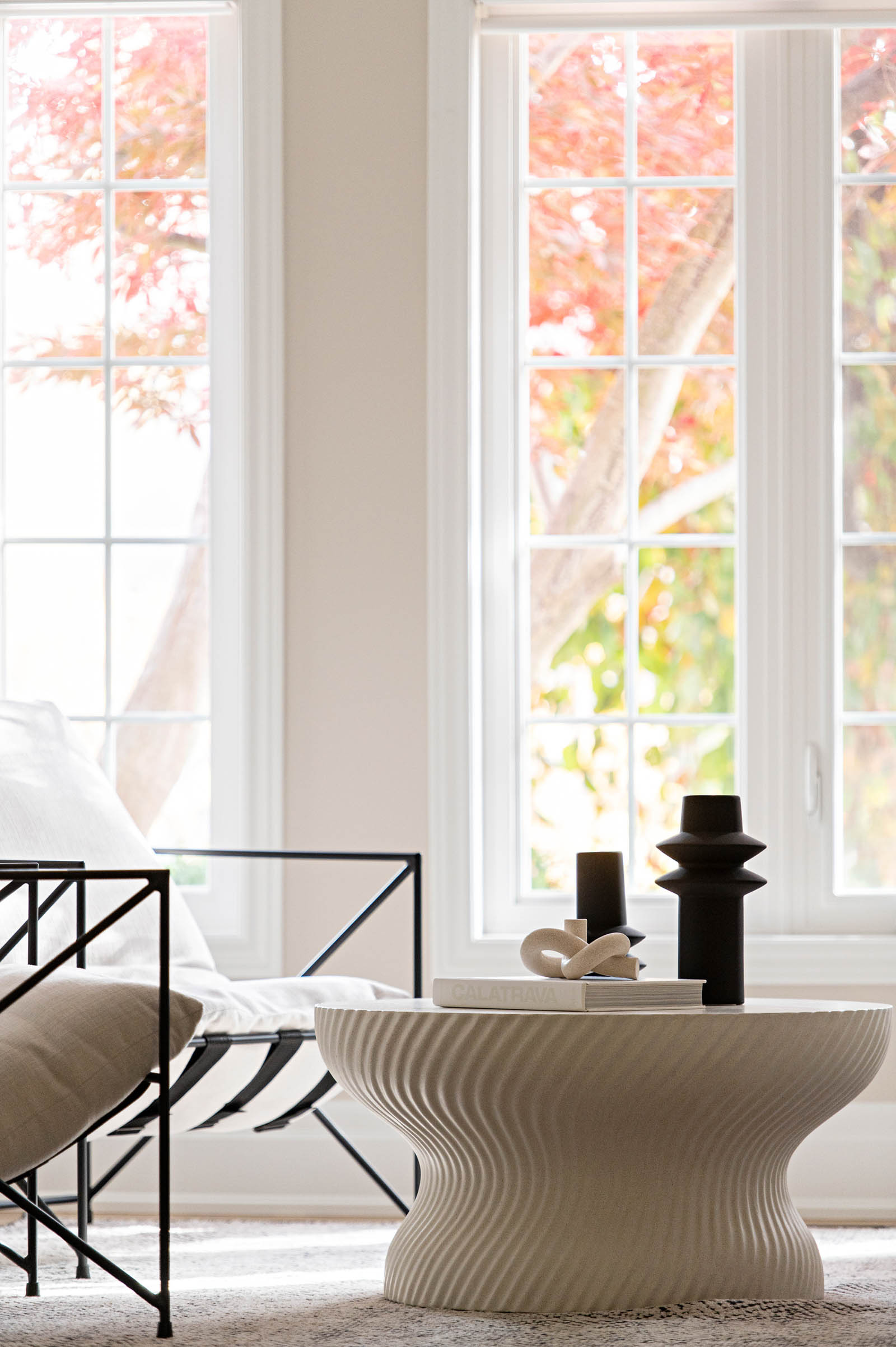 Image of Modern living room with two white lounge chairs with metals arms and textured white coffee table and area rug.