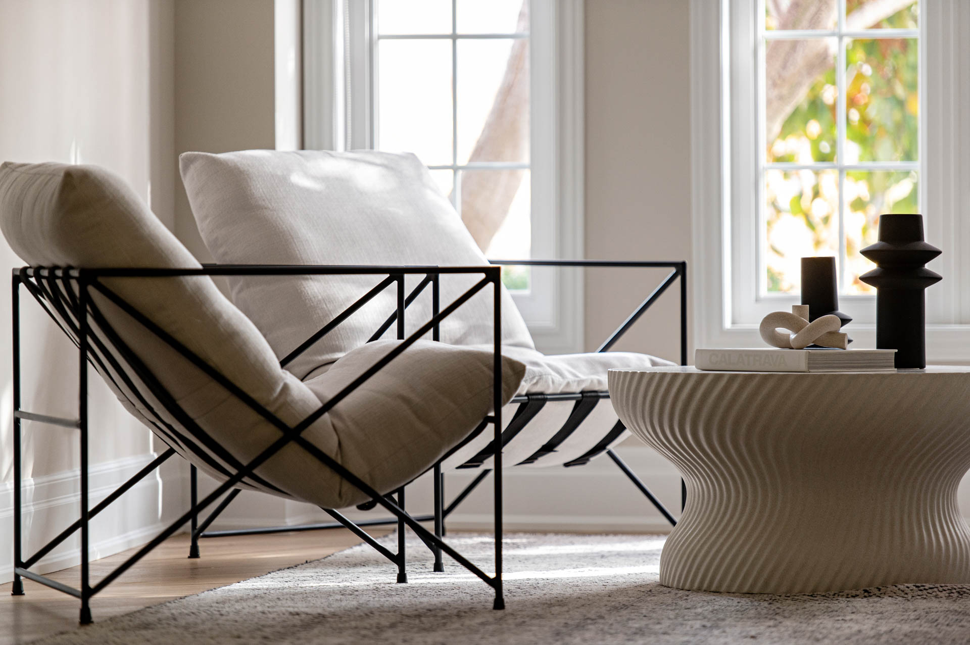 Image of modern living room with two white lounge chairs with metals arms and textured white coffee table and area rug.