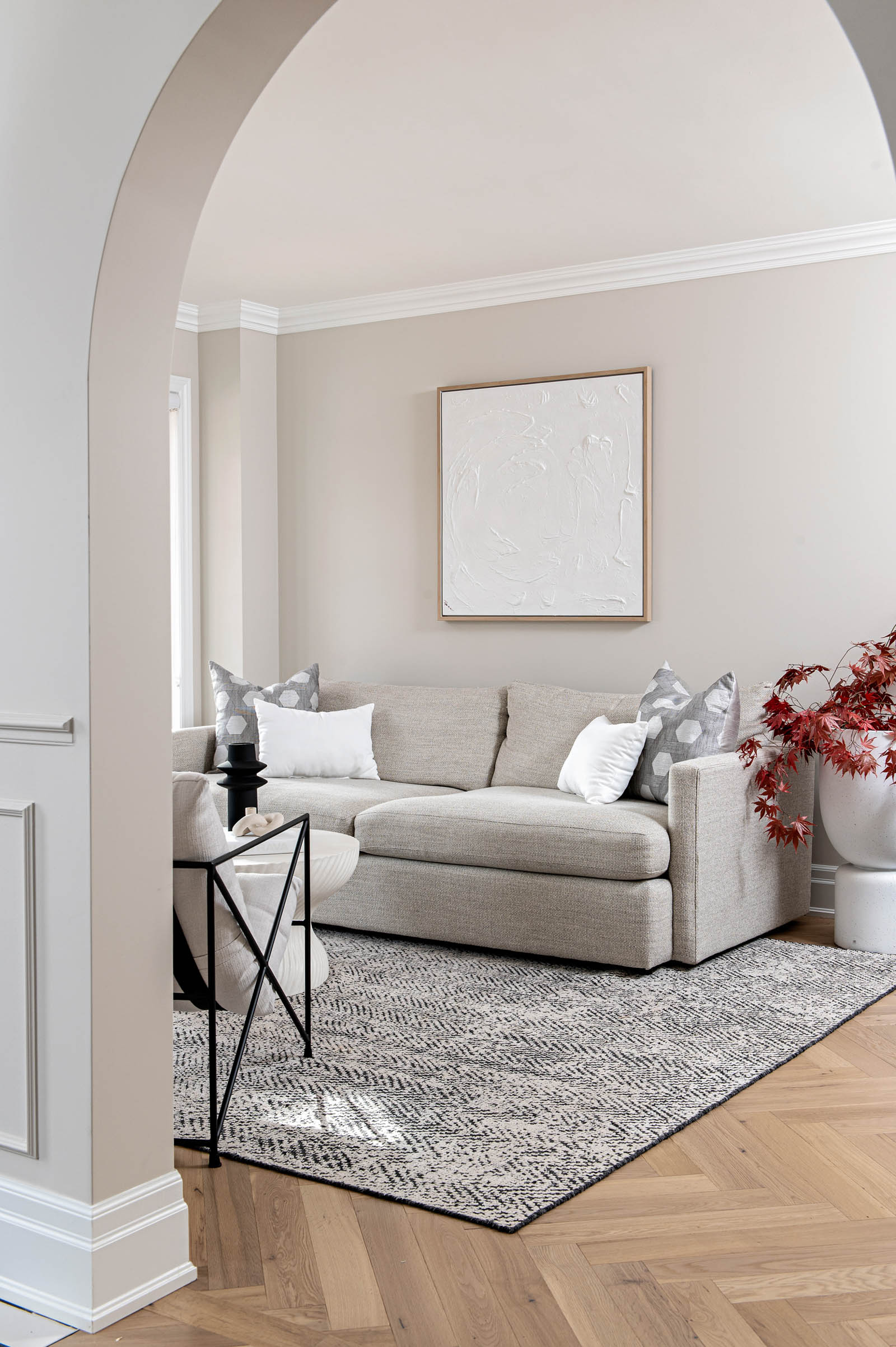 Image of Living Room looking in from front entrance, showcasing a light sofa, textural black and white area rug, textured white art.