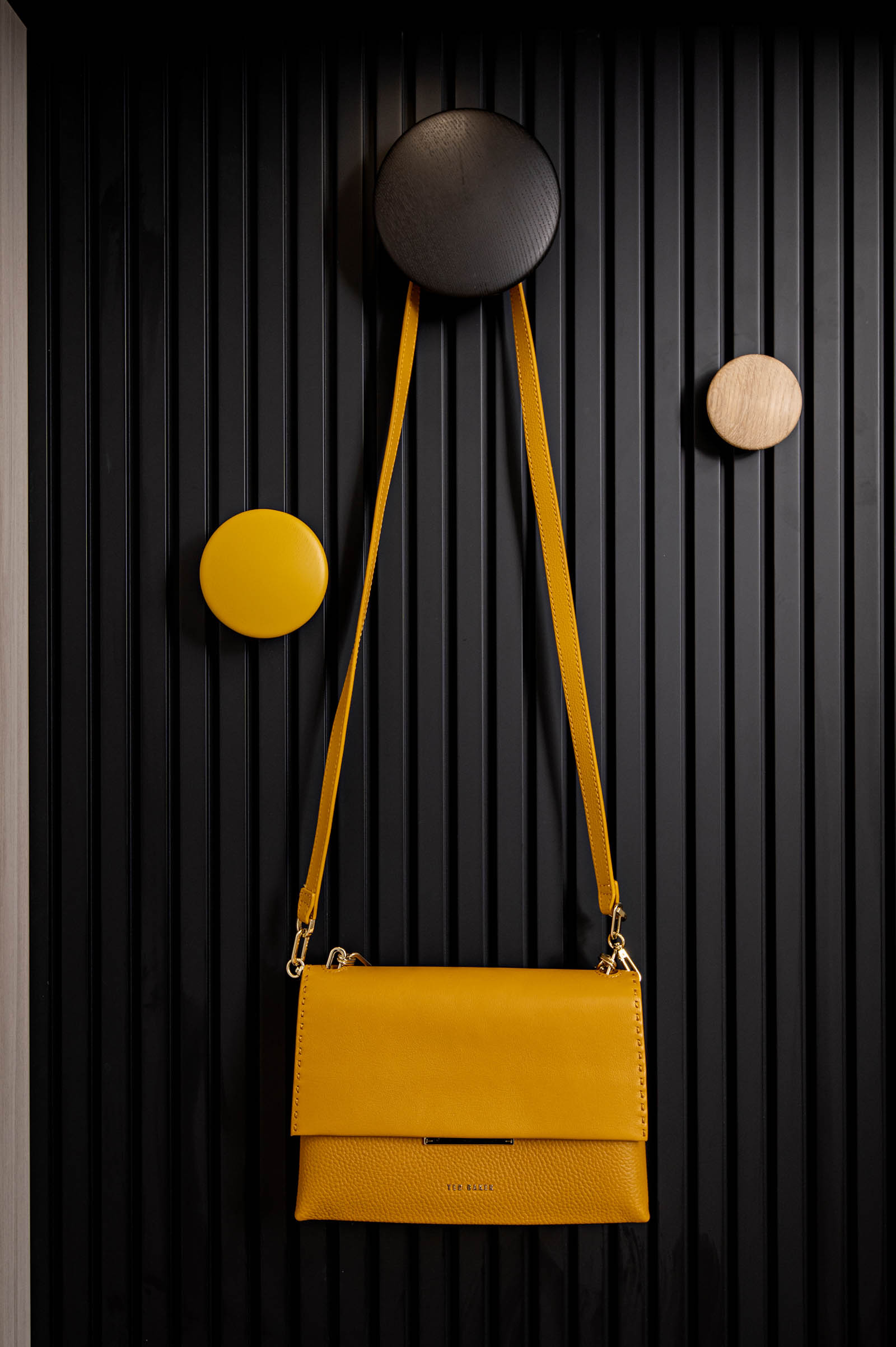 Closeup image of Muuto wood wall hooks on black reeded wood wall in mudroom.