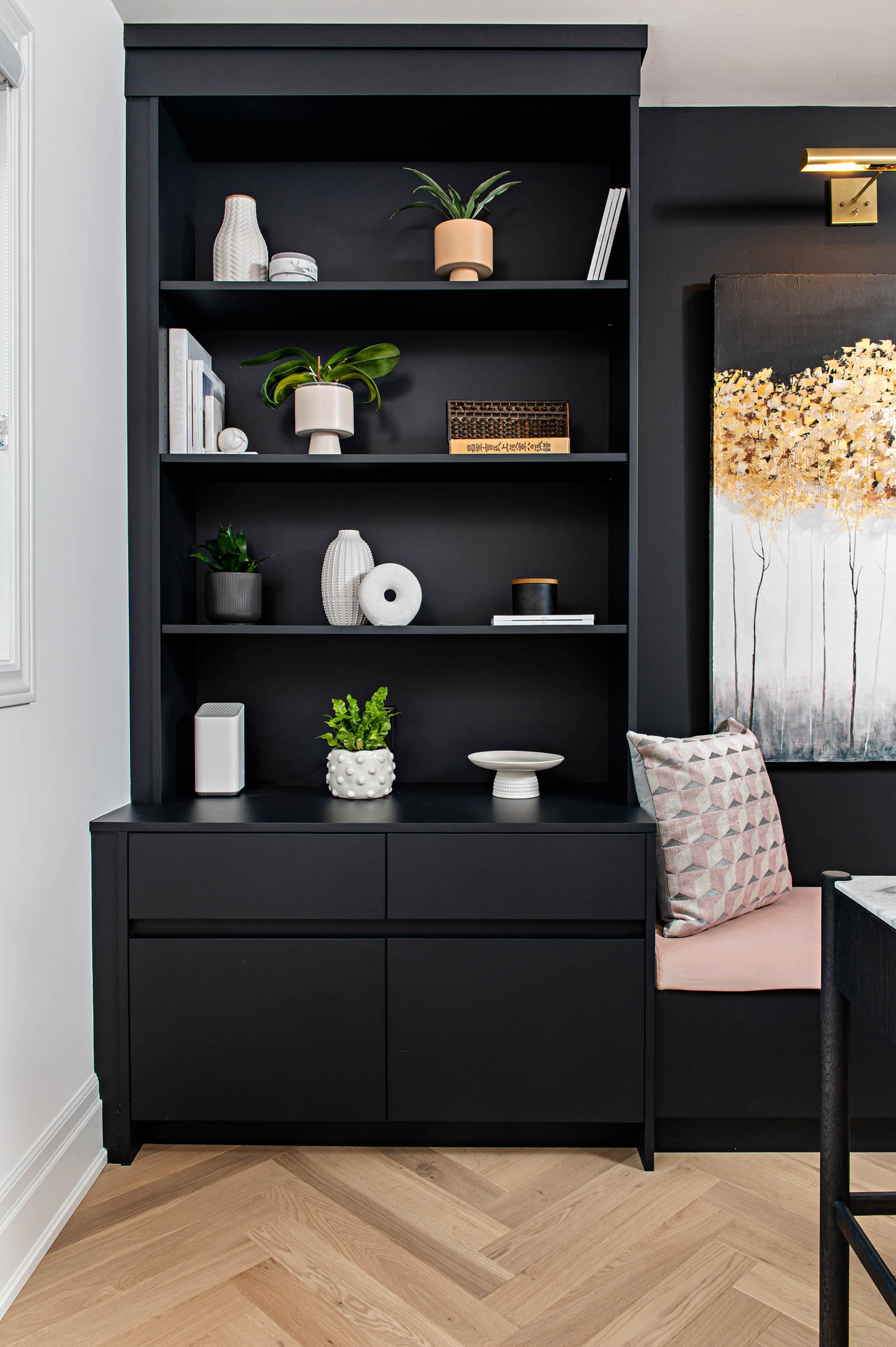 Image of custom built home office black shelving, open shelf and bottom filing storage, beside it a bench with upholstered pink fabric and artwork above.