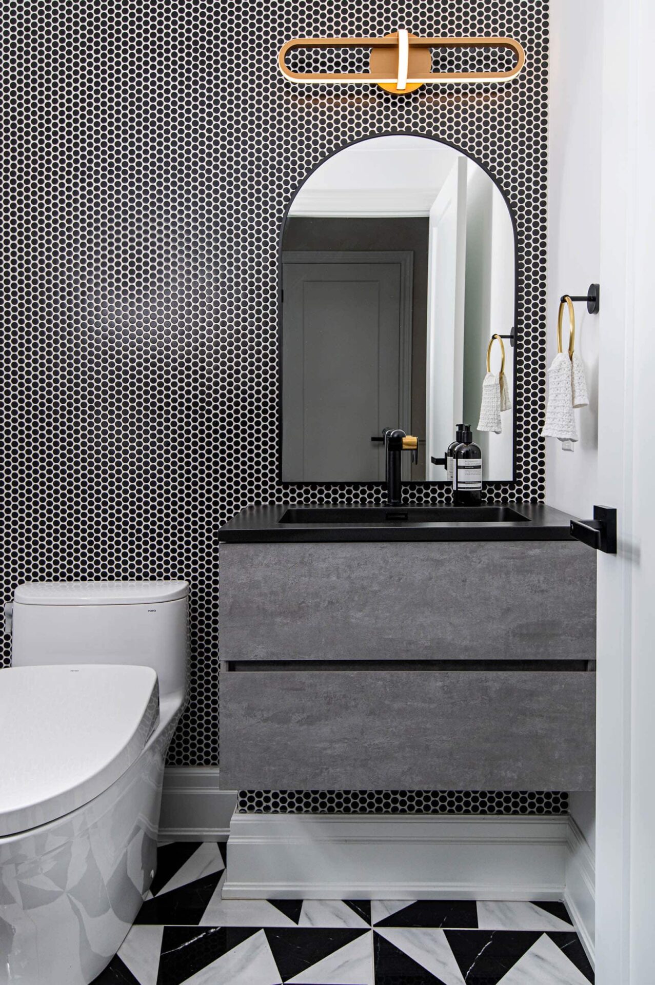 Image of a Powder Room design with black penny tile wall, geometric black and white porcelain floor, floating vanity.