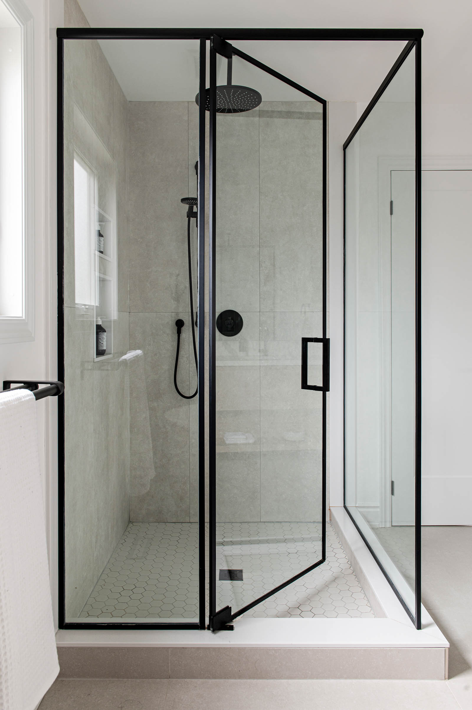 Image of master ensuite shower with black framed glass enclosure, rainfall shower head, concrete like tile.