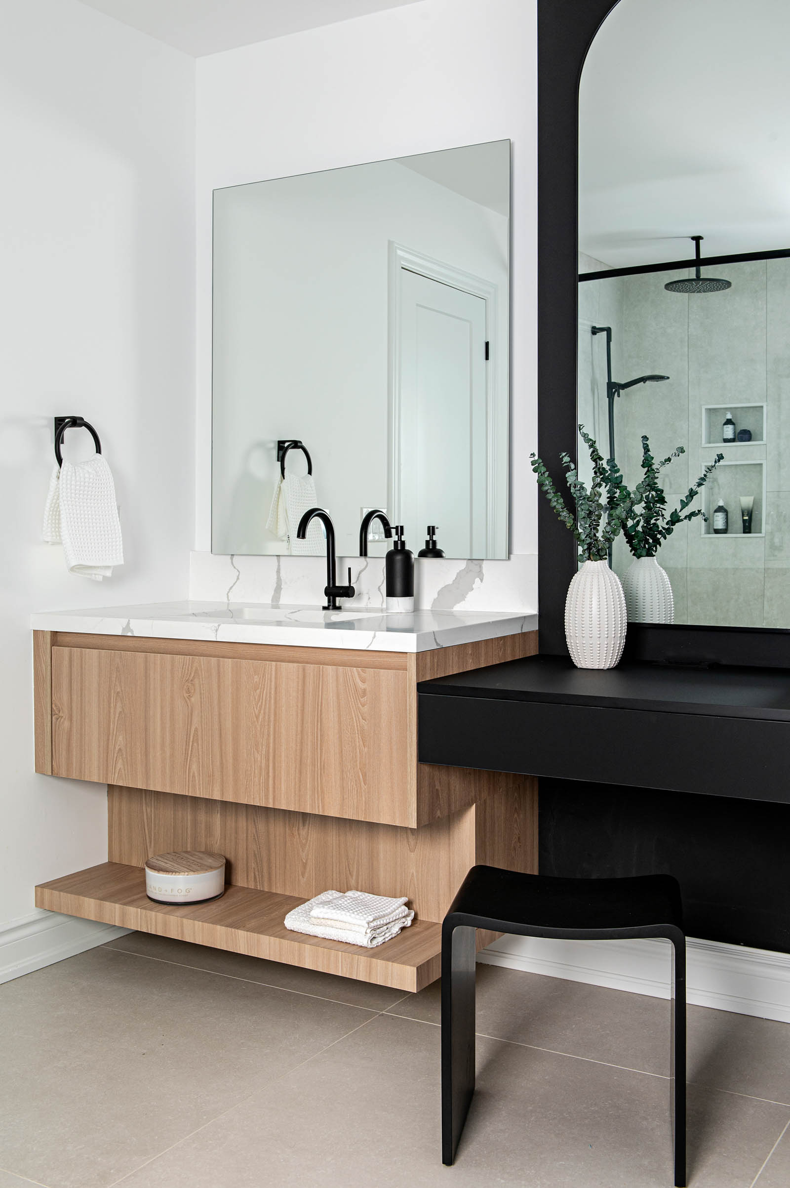 Image of a contemporary primary ensuite bathroom, showcasing a wood floating vanity with shelf and white quartz countertop, backlit mirror, black makeup vanity.