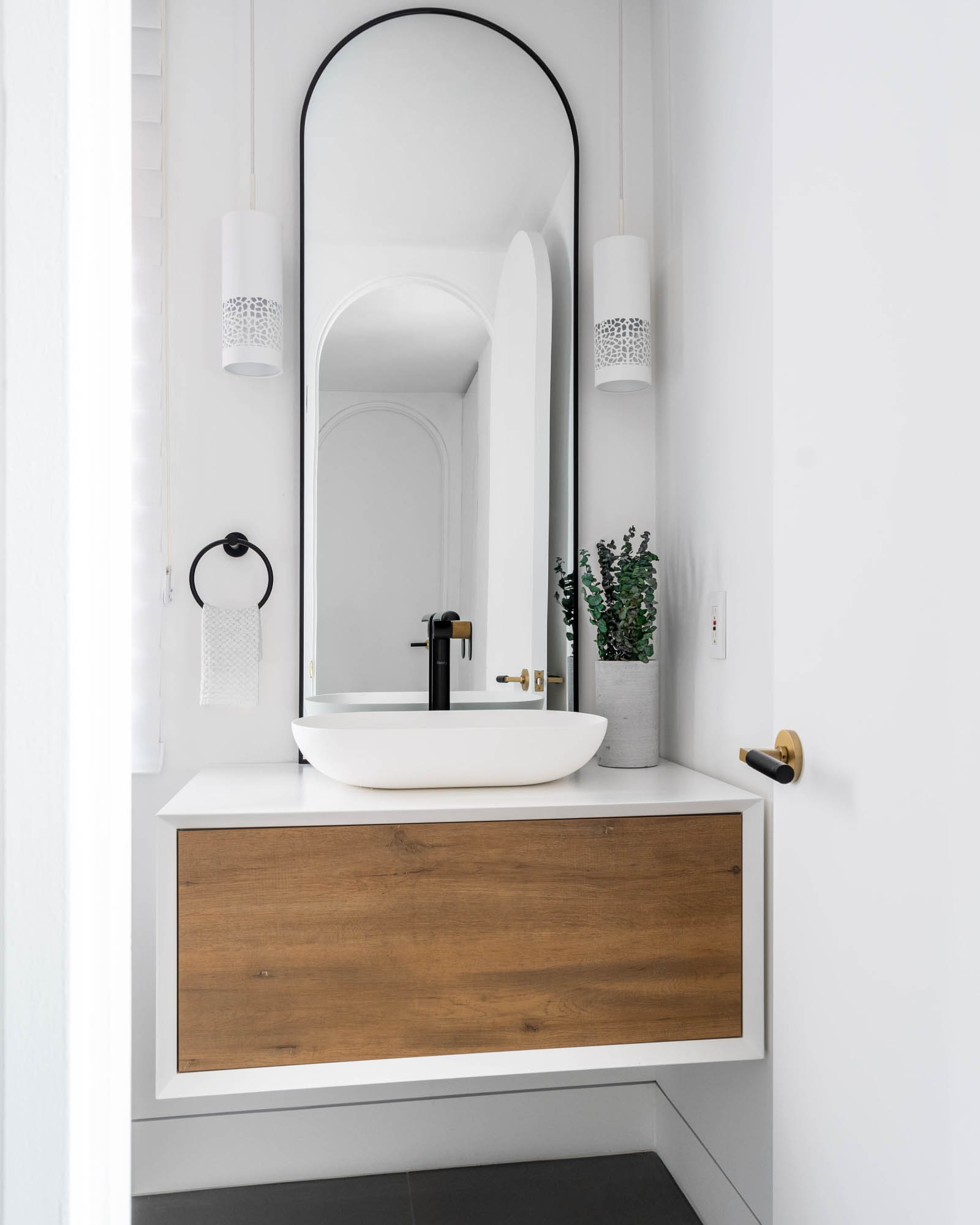 Image of a contemporary guest bathroom renovation, showcasing a sleek floating vanity, modern vessel sink, large curved mirror, and stylish black and gold faucet.