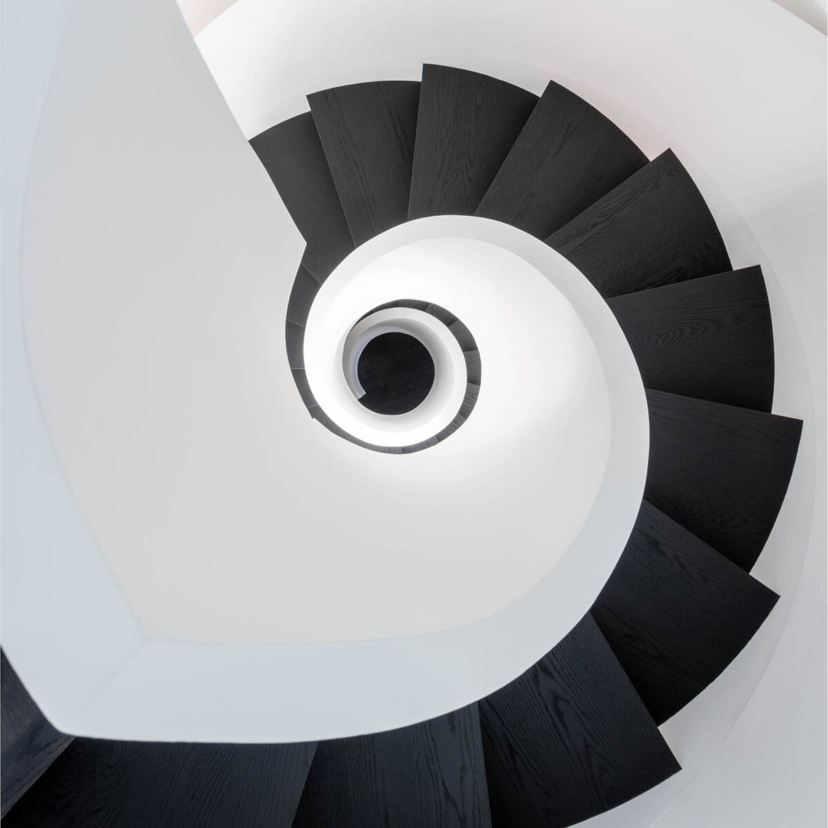 Image of a Contemporary curved staircase view from second floor to basement, black engineered hardwood and white drywall railing. Basement renovation Toronto curved staircase with modern black steps and clean white structure.