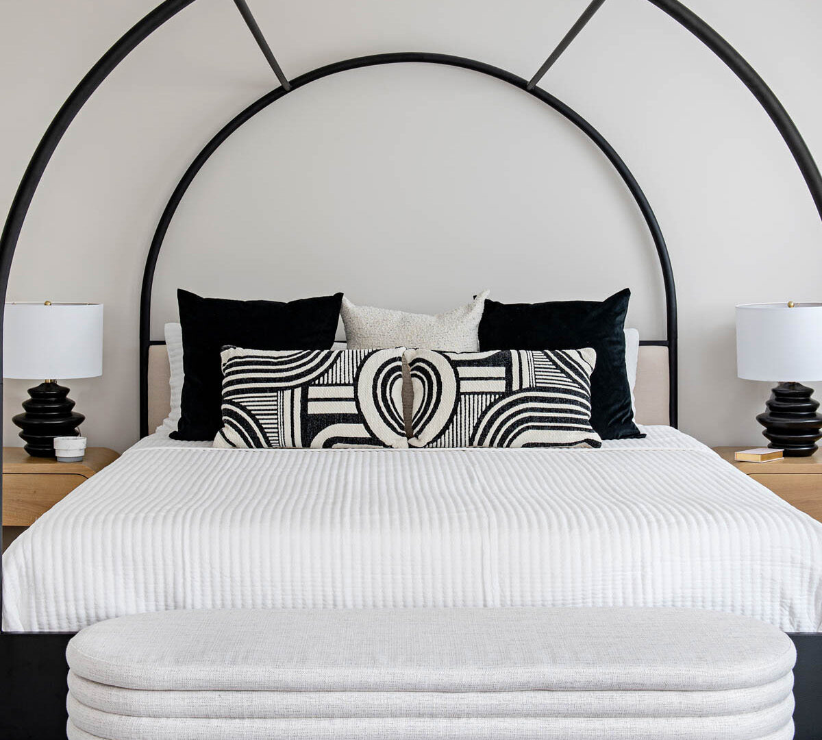 Image of Black and White Decor Primary Bedroom, black metal arched canopy bed with natural wood side tables, black table lamps.