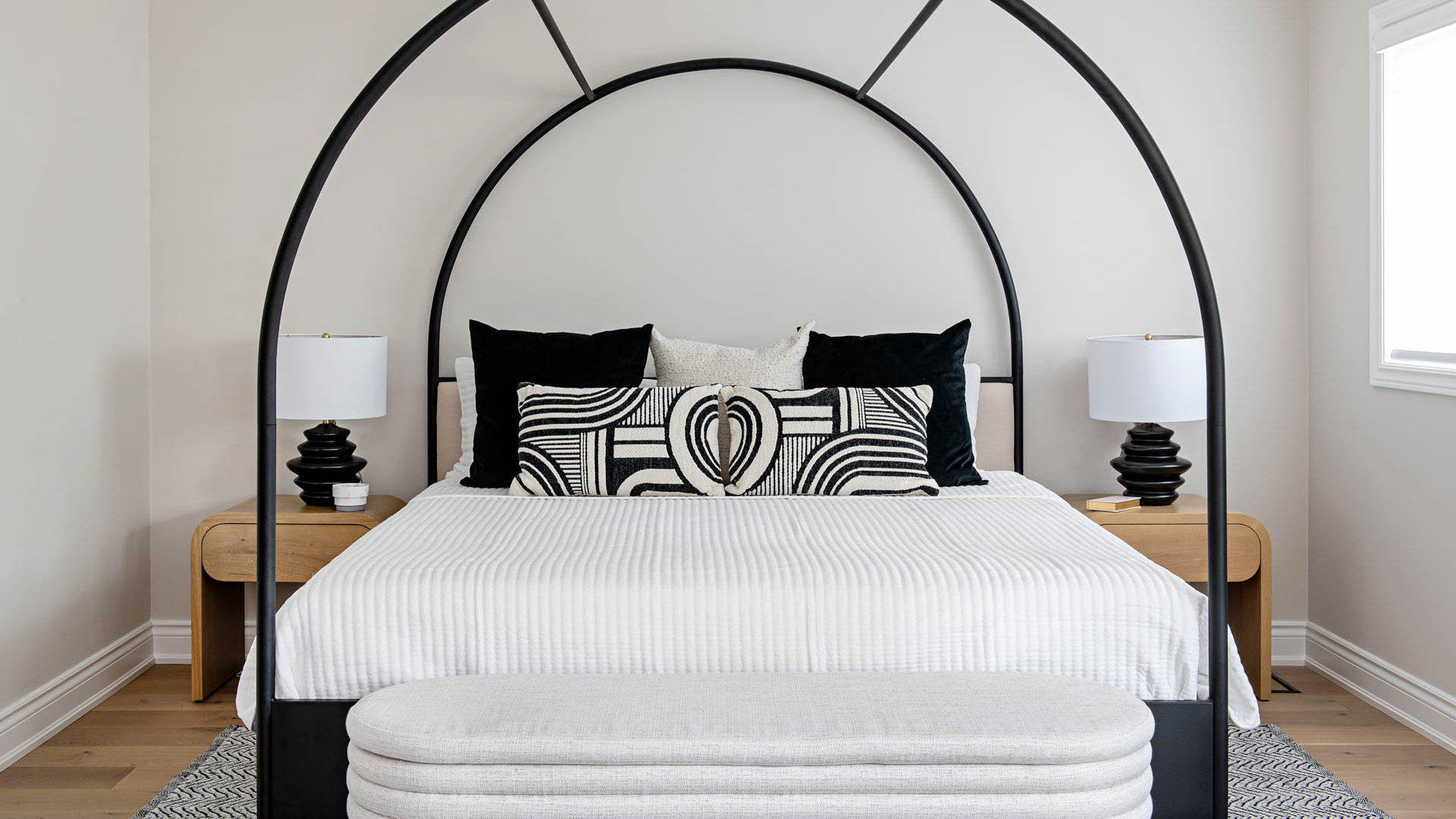 Image of Black and White Decor Primary Bedroom, black metal arched canopy bed with natural wood side tables, black table lamps.