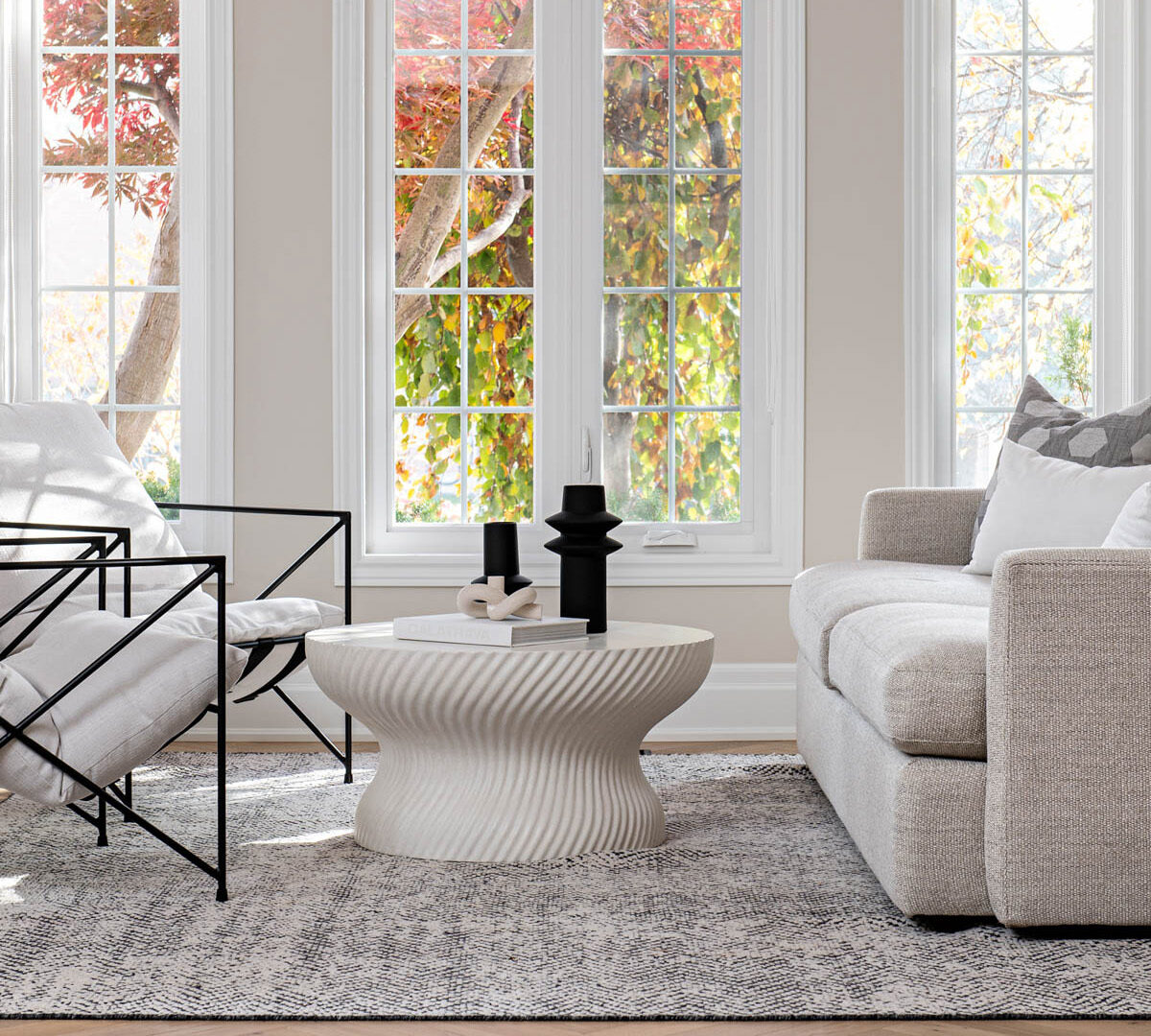 Image of Modern white living room arranged with sofa, coffee table, two lounge chairs, anchored by area rug.