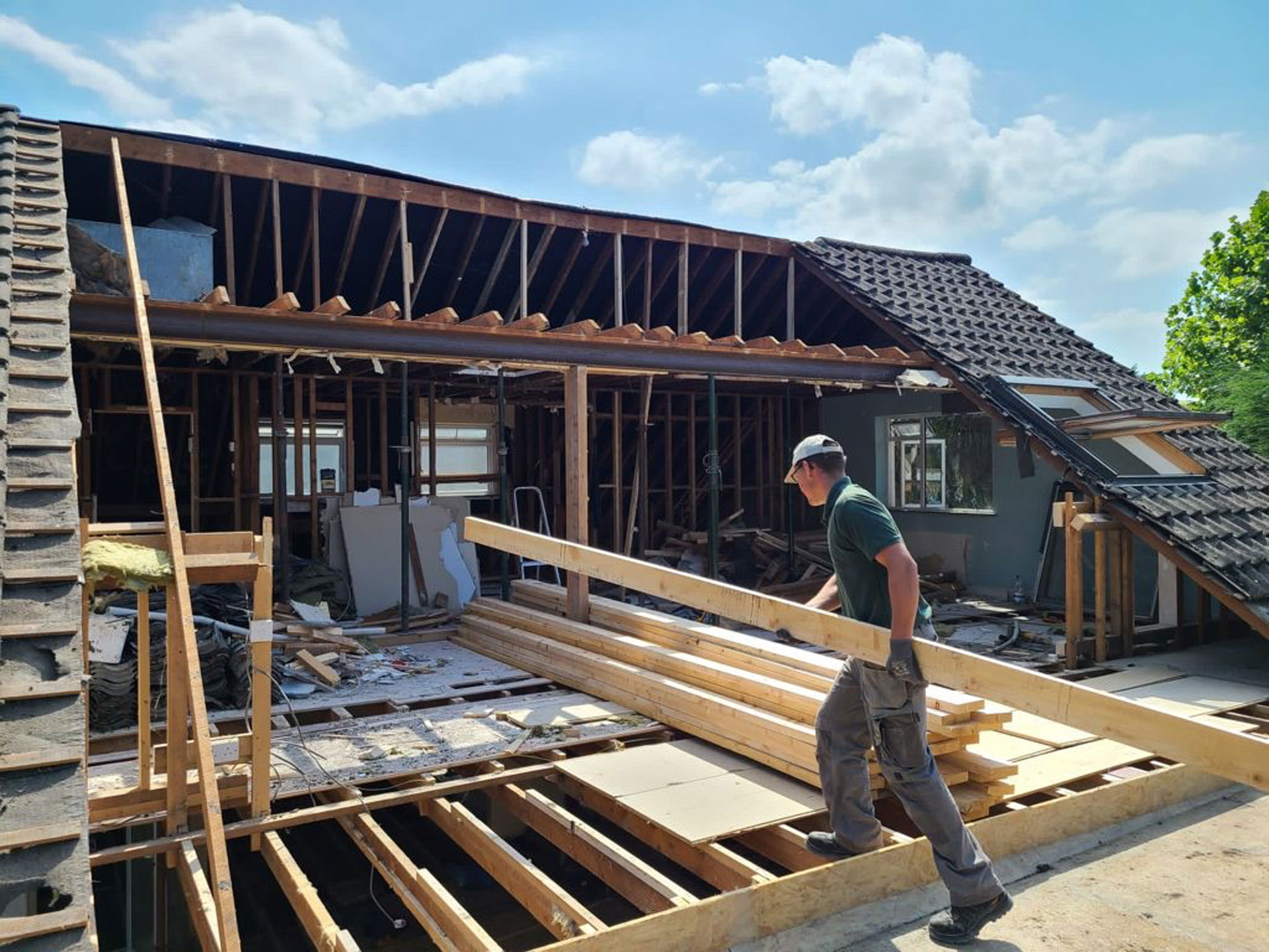 Construction worker carrying wooden beams at a renovation site of a Dublin residence, with a partially deconstructed roof.