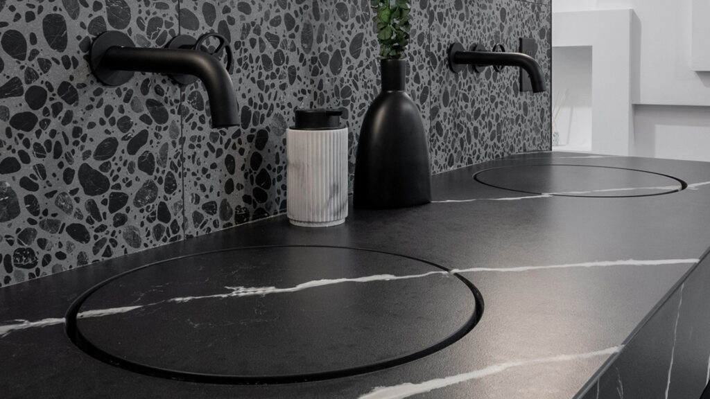 Modern bathroom countertop with sleek black fixtures and a stylish terrazzo backsplash.