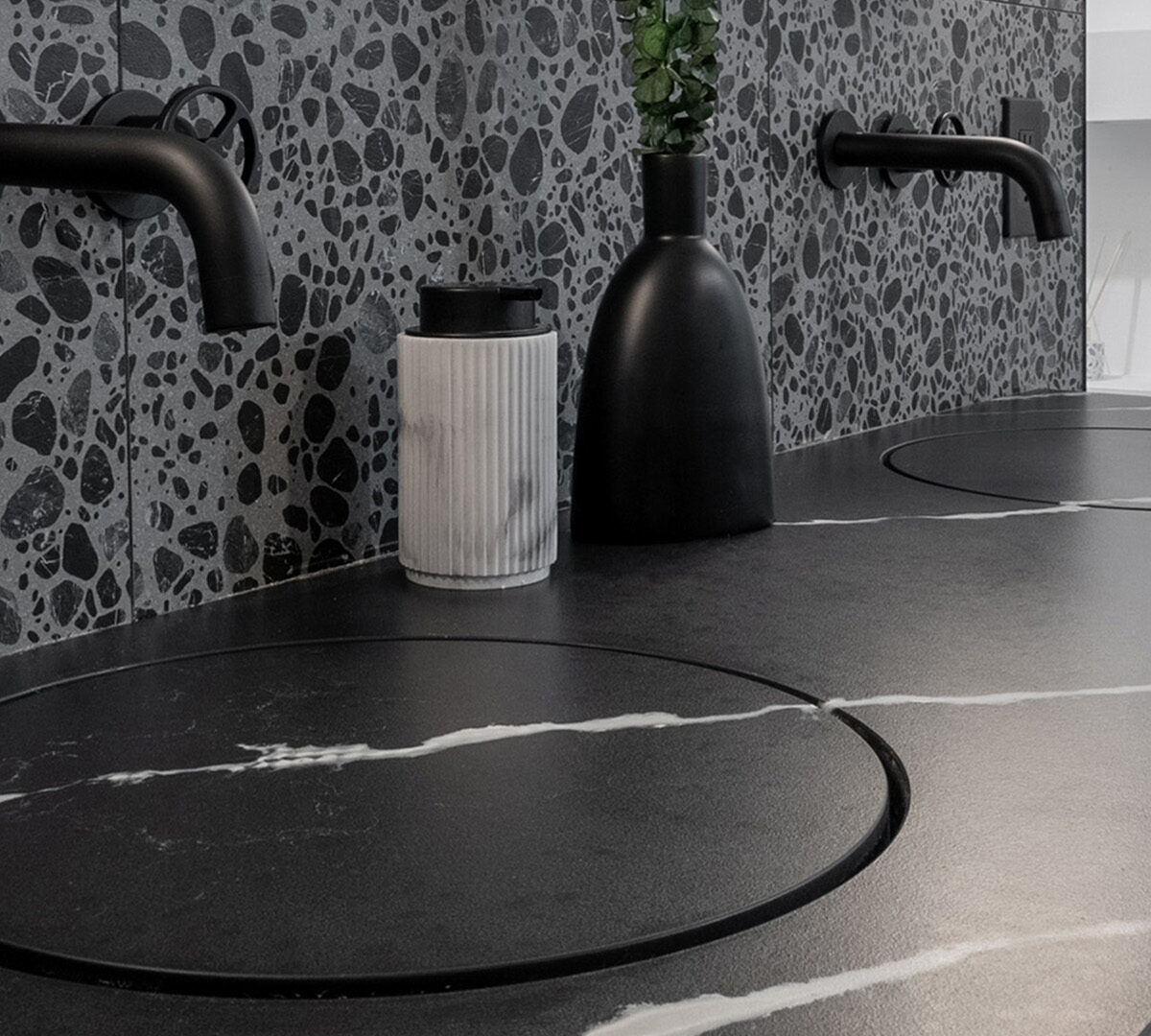 Modern bathroom countertop with sleek black fixtures and a stylish terrazzo backsplash.