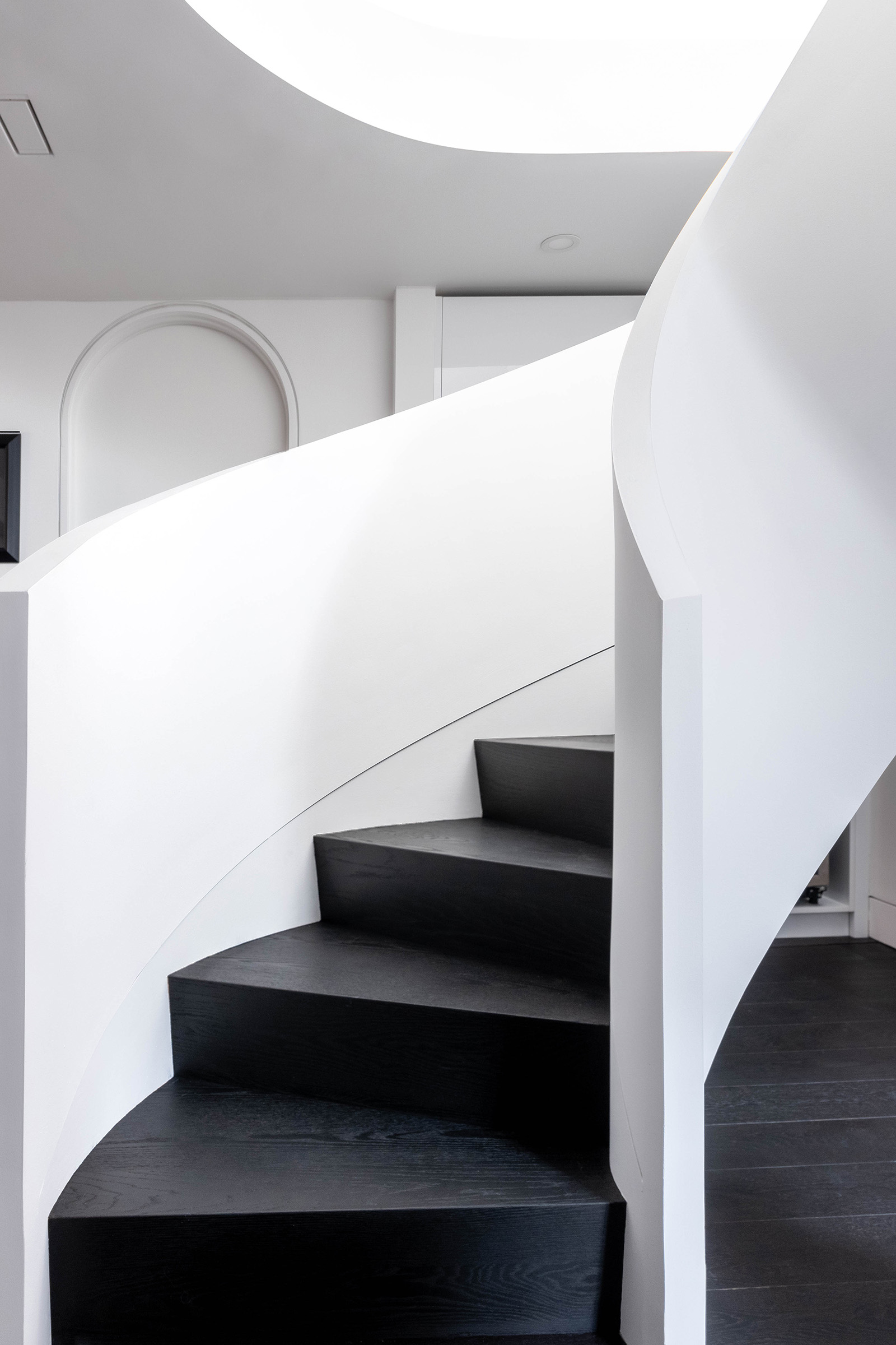 Modern curved staircase with stained black steps and white walls.