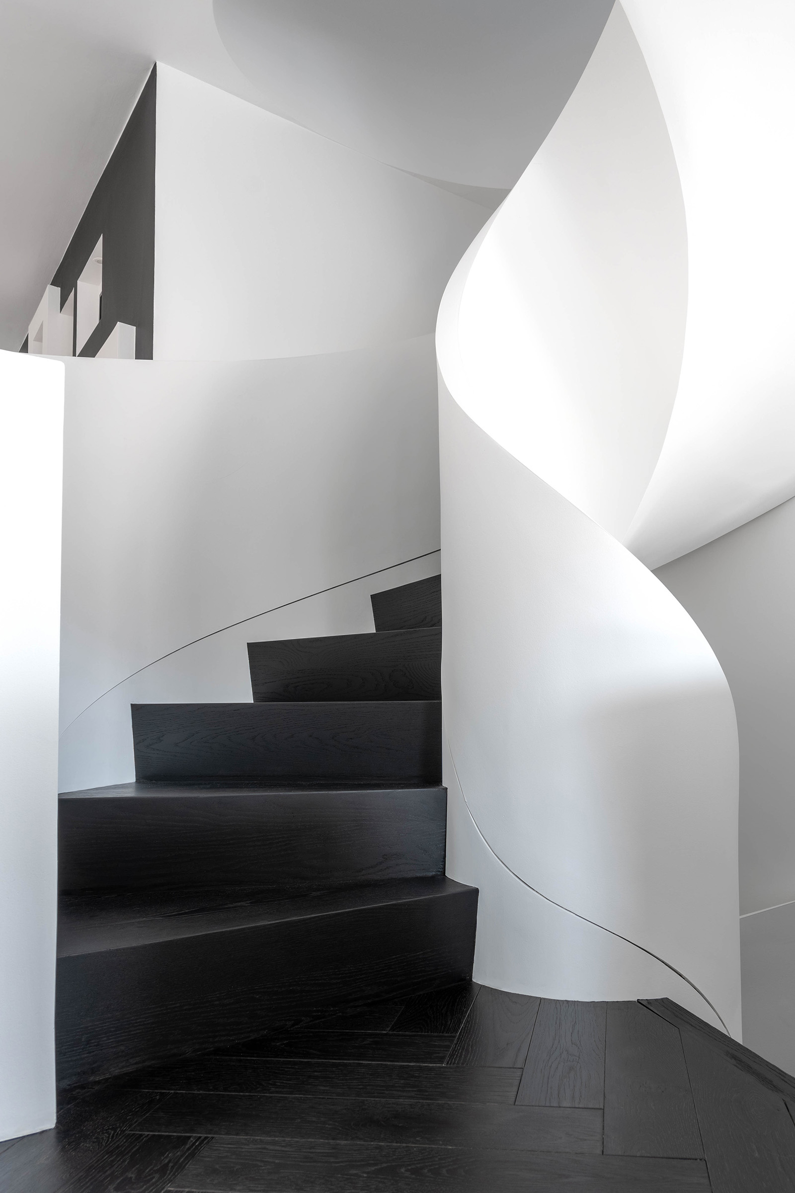 Curved staircase with stained black steps and white walls on the main floor.